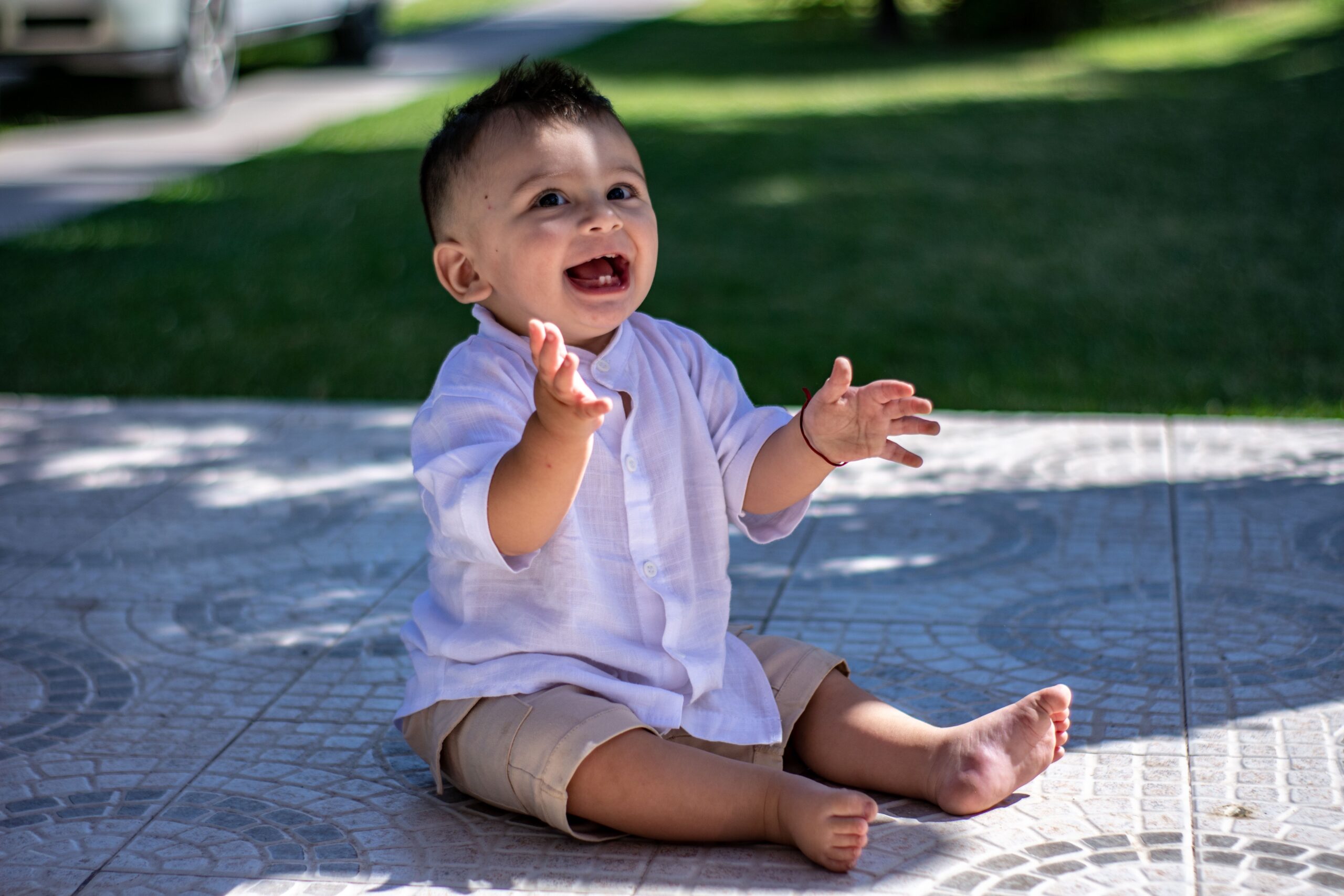 Cute toddler sitting happily in casual summer outfit, enjoying a sunny day outdoors.